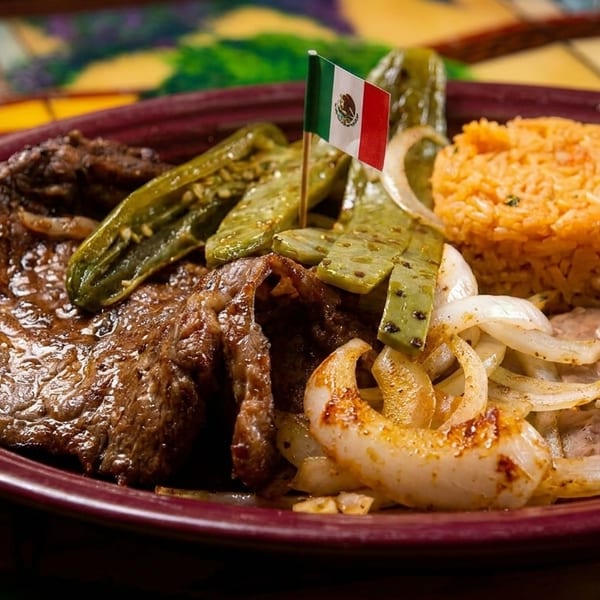 Mexican steak dish with rice, beans, grilled onions, nopales, and a small Mexican flag.