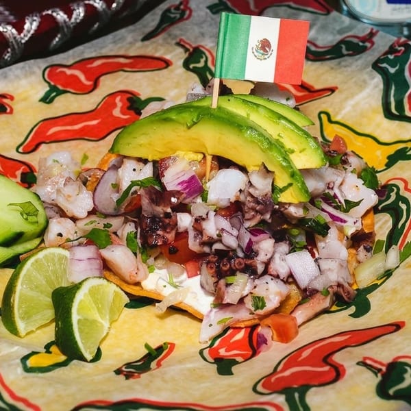 Mexican ceviche with octopus, shrimp, avocado, and lime on chili-patterned paper.