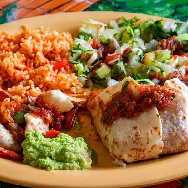 A vibrant Mexican plate with burritos, rice, salad, and guacamole on a colorful table.